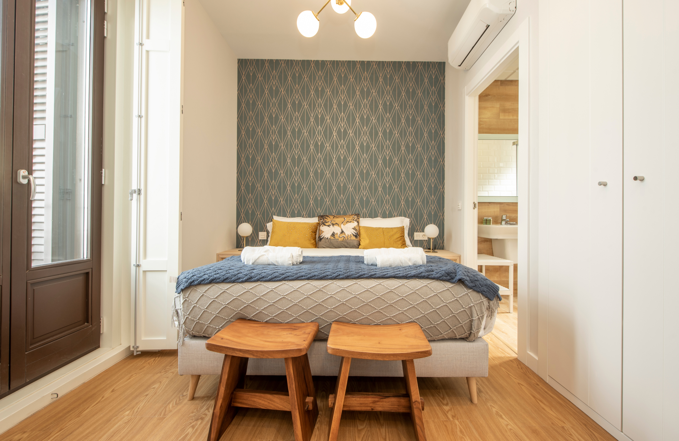 Comfortable studio apartment bedroom with a stylish bed, natural light, warm wood finishes, and compact design.
